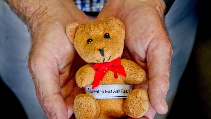 A man holds a small teddy bear in the palm of his hands