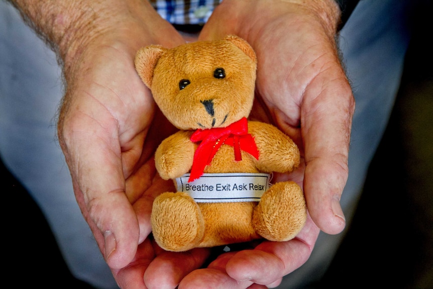A man holds a small teddy bear in the palm of his hands