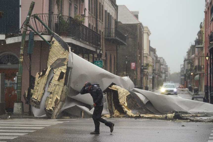 A man passes by a section of roof that was blown off of a building by Hurricane Ida winds