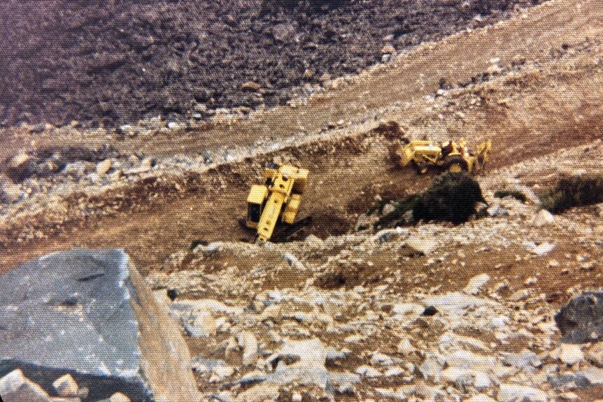 Yellow digger building road in rocky steep landscape
