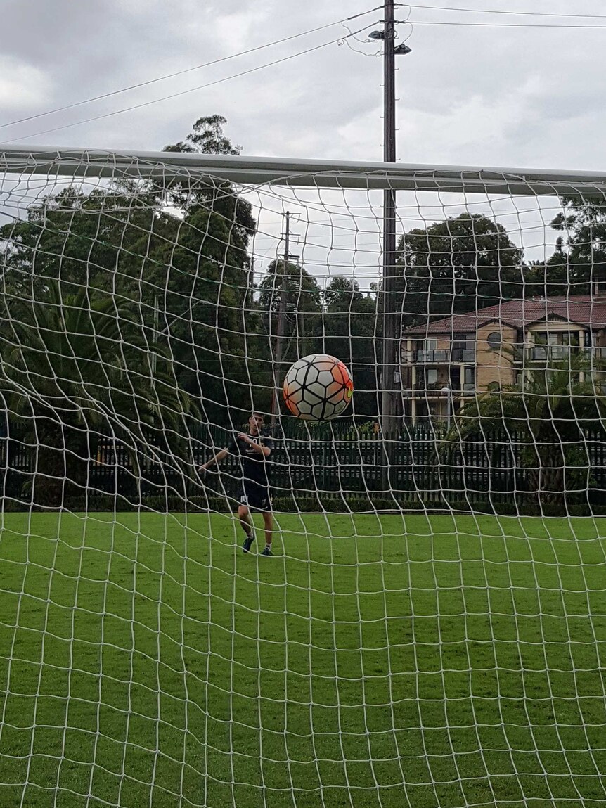 soccer goal net from behind with a ball coming towards it and a player in the far background