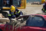 A firefighter crouches down on the bonnet of a car and looks in the window. 