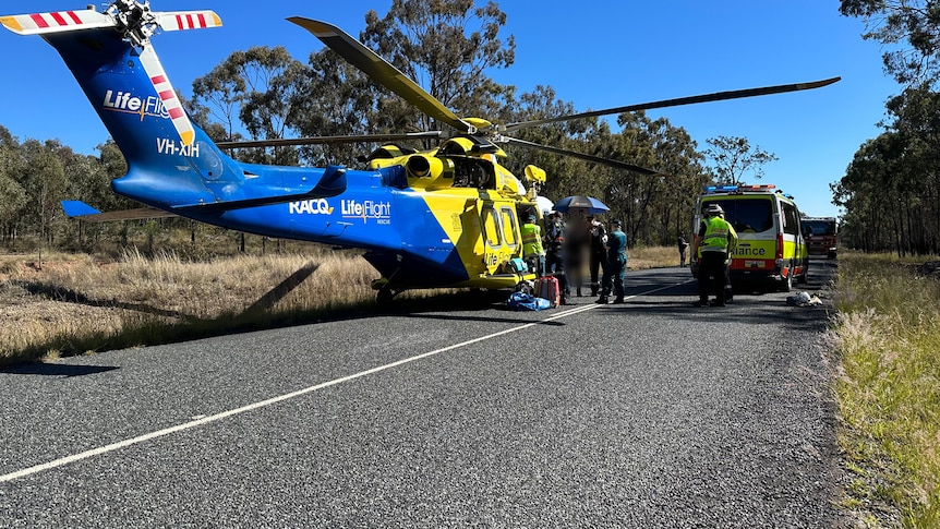 A helicopter on a stretch of rural road next to an ambulance. 