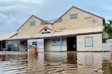 Image of an old, corrugated iron building, with flood water in the foreground.