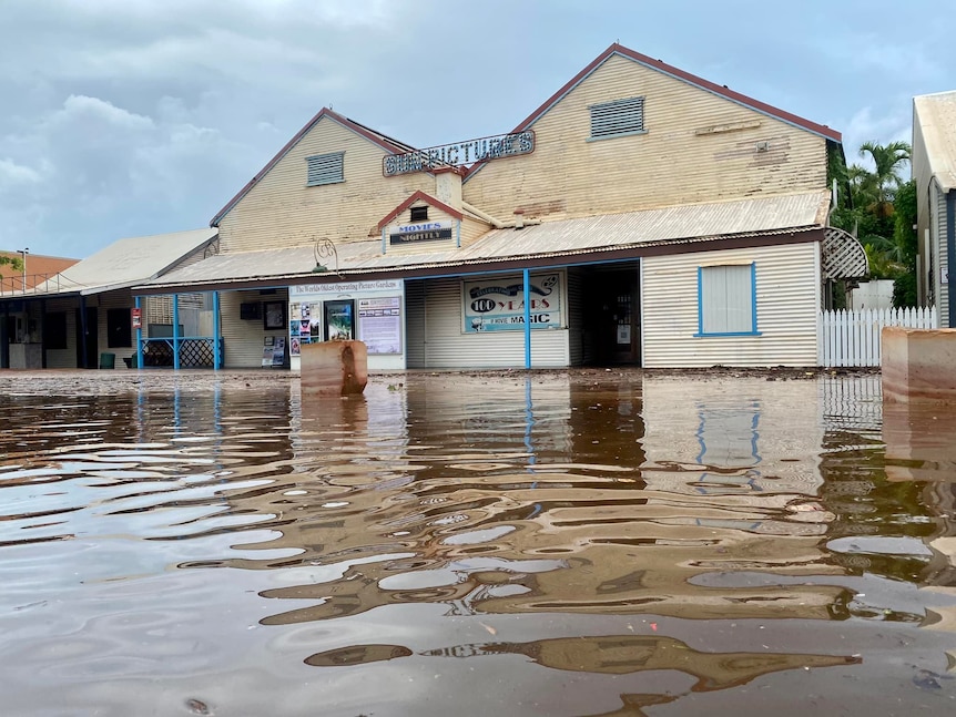 Image of an old, corrugated iron building, with flood water in the foreground.