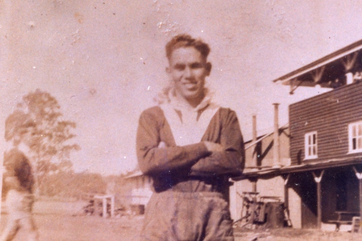 Sepia photo of Indigenous man in a shirt and shorts and his arms folded.