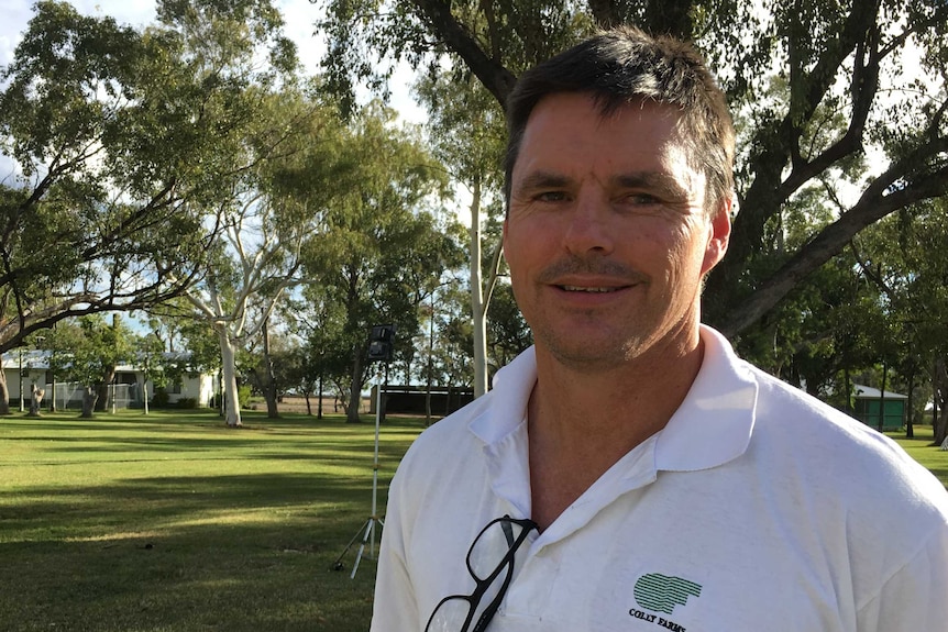 David Statham stands in a yard with trees, smiling at the camera