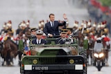 Emmanuel Macron waves as stands in the military command car.