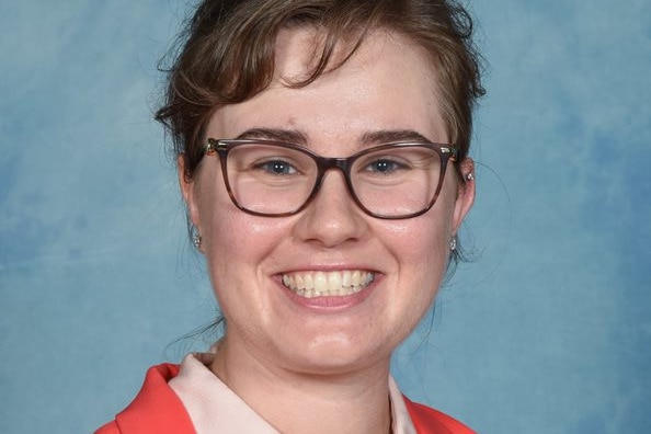 Head shot of  Krystal Gagen-Spriggs in orange jacket in front of a blue background