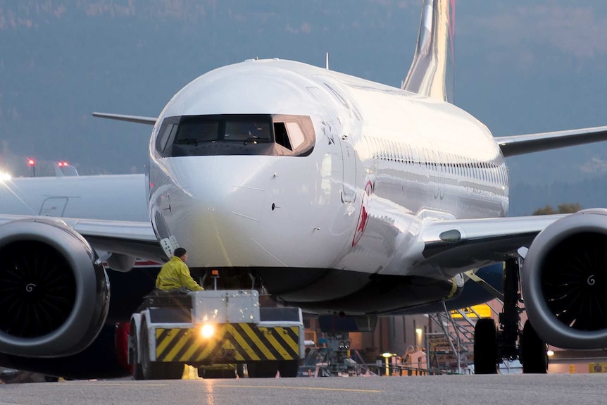 An Air Canada Boeing 737 MAX 8 is pictured close-up, while being carried by a vehicle-tug flashing its lights on the tarmac.
