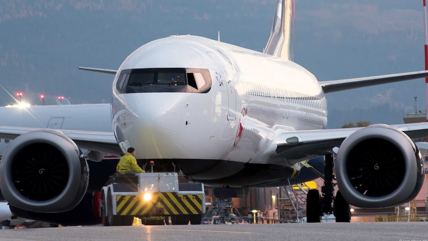 An Air Canada Boeing 737 MAX 8 is pictured close-up, while being carried by a vehicle-tug flashing its lights on the tarmac.