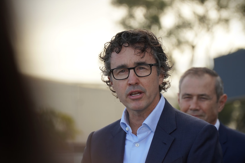 Man with dark curly hair and glasses speaking.