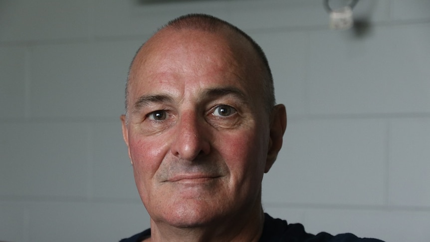 Close up photo of middle-aged bald man staring at camera with green-brown eyes and slight smile.