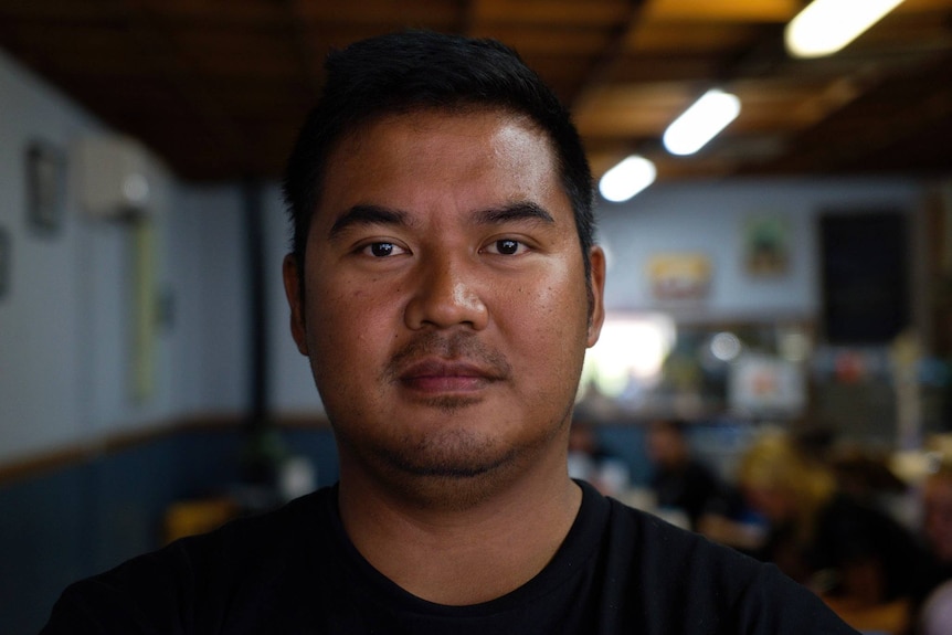 Man with black hair looking at camera with cafe in background 