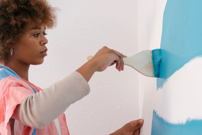 A woman paints a blue line on a blank wall