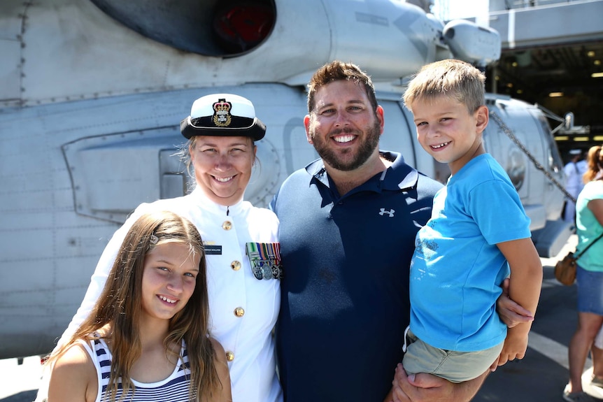 A family embrace while standing on a dock in front of a large navy vessel