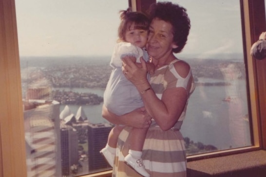 Grainy faded colour photo of an older woman smiling, holding a small child very close to her.