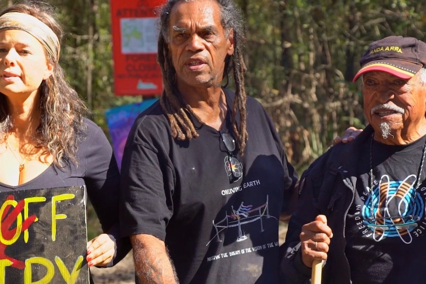 Gumbaynggirr elders stand together with a woman holding a placard protesting logging in Newry State Forest 