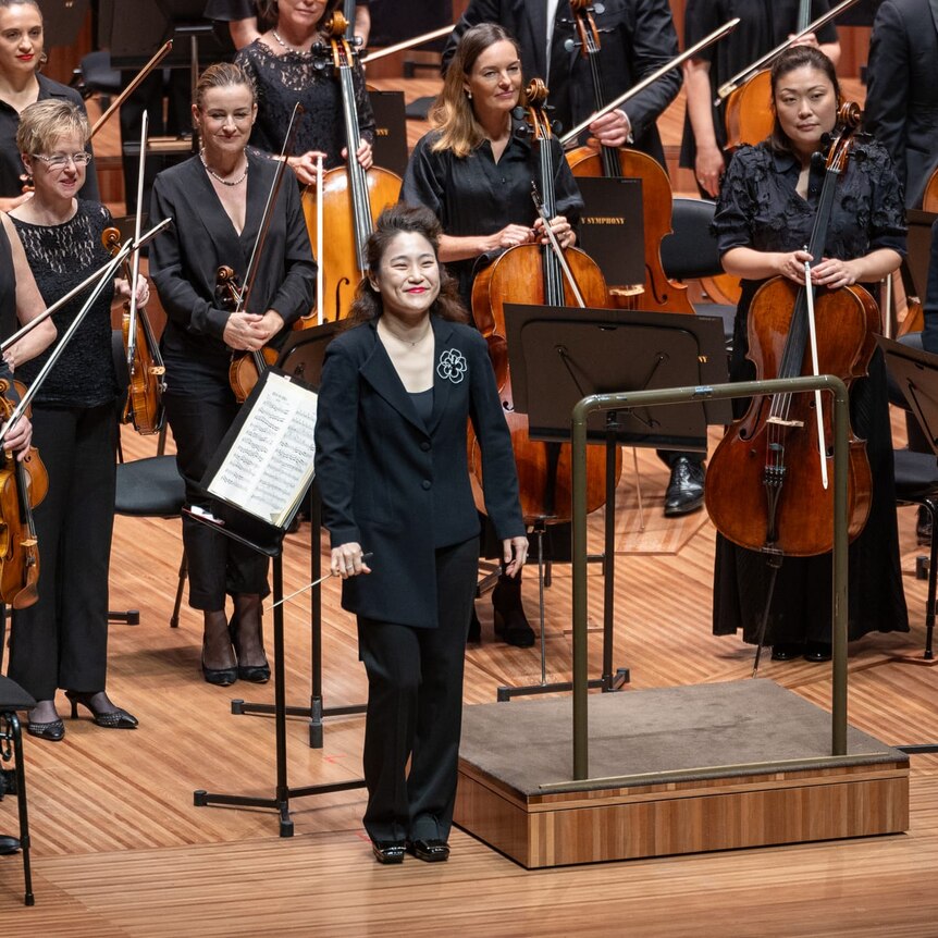 Ha-Na Chang stands in front of the Sydney Symphony Orchestra on stage at the Sydney Opera House Concert Hall