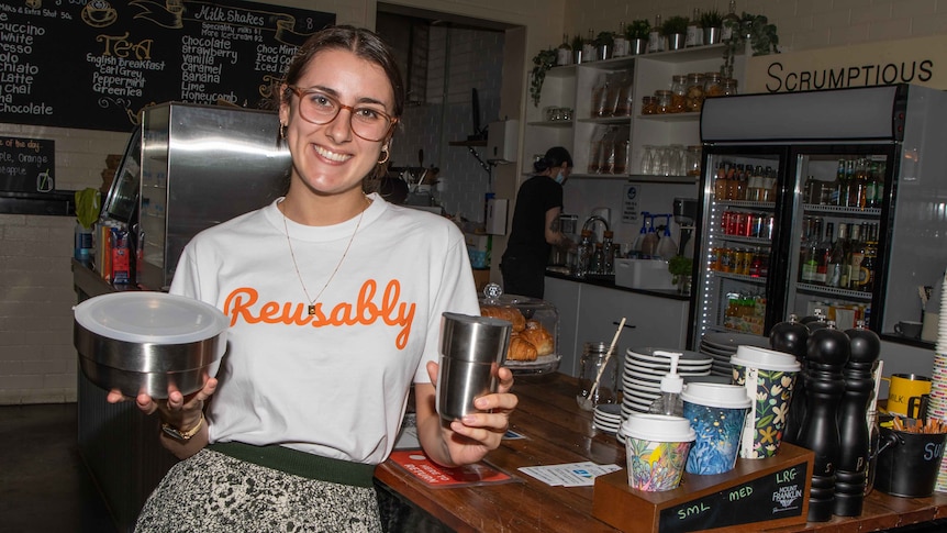 woman stands in cafe holding the reusable products 