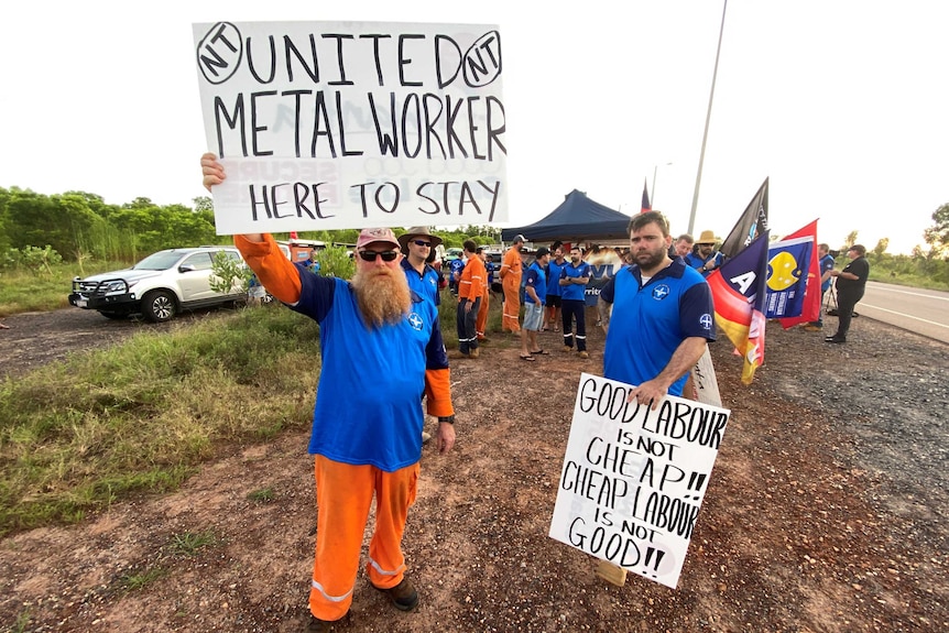 Men in high-vis holding protest signs by the side of the road.