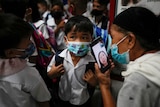 A boy wearing a mask on his first day of school talks to his mother on a smartphone video call.