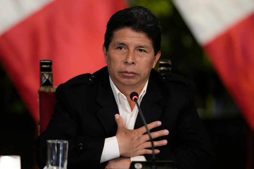 pedro castillo speaks into a desk microphone with his hand on his chest