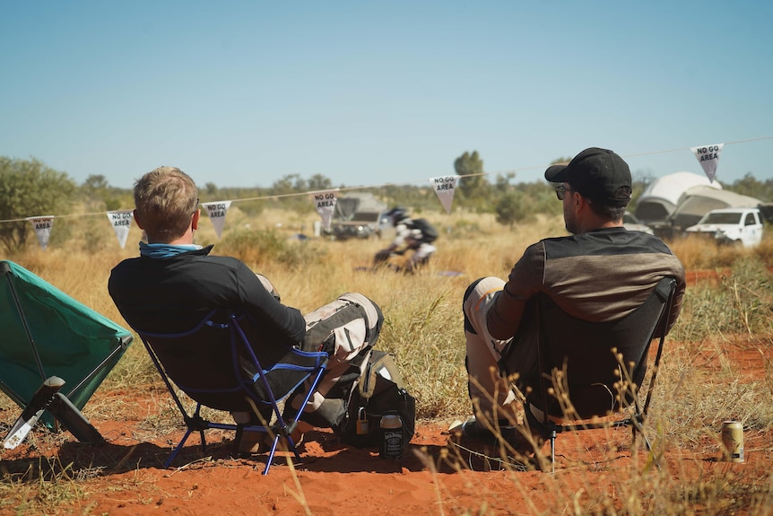 Two men sitting in camp chairs behind flags that say "no-go area".