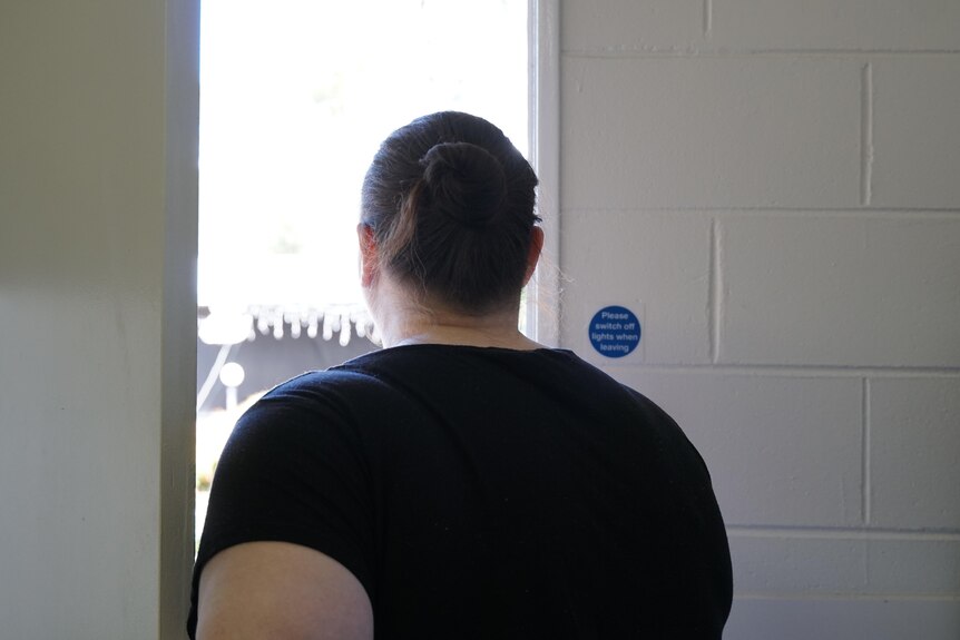 A woman in a black top standing with her back to the camera looking out of a door