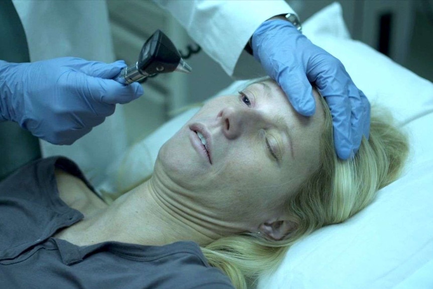 Gwyneth Paltrow looking unwell while a doctor shines a light in her eye