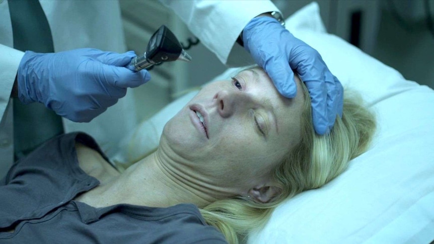 Gwyneth Paltrow looking unwell while a doctor shines a light in her eye