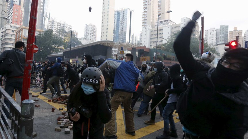 Protestors throw bricks in a large crowd as journalists take cover
