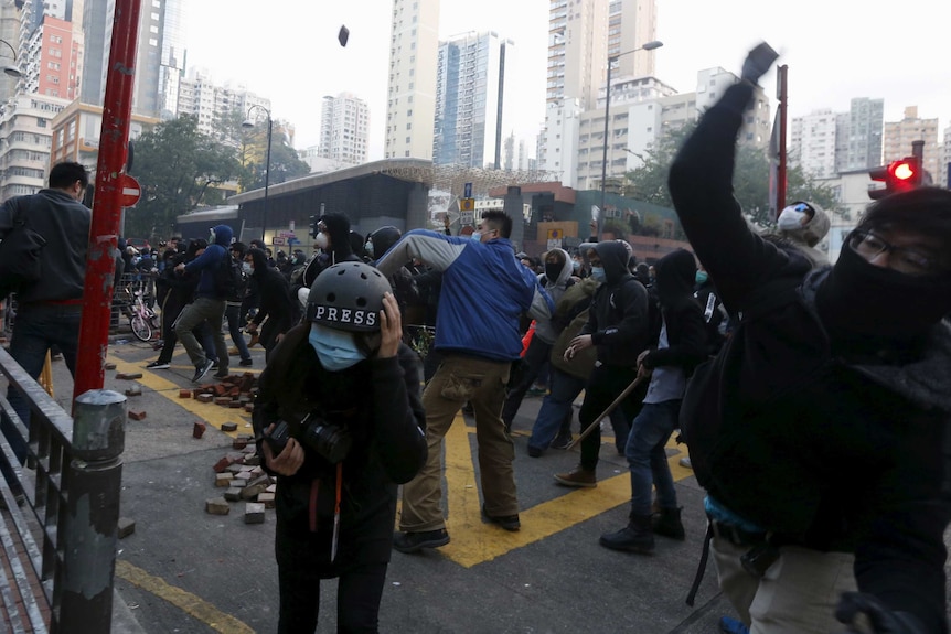 Protestors throw bricks in a large crowd as journalists take cover