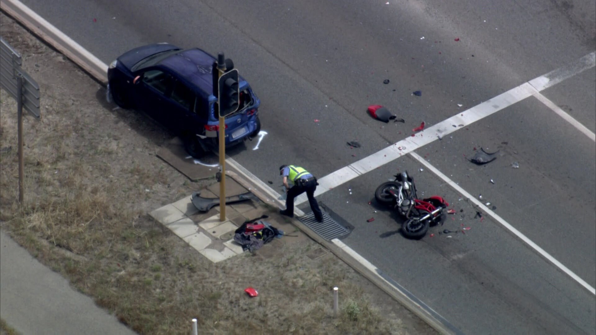 A smashed up motorcycle lies on its side behind a blue car at a traffic light