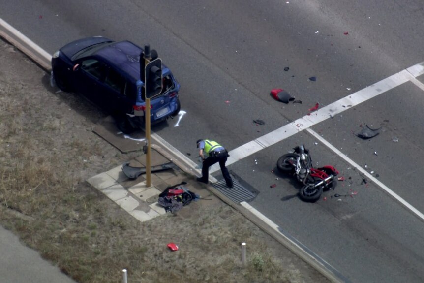 A smashed up motorcycle lies on its side behind a blue car at a traffic light