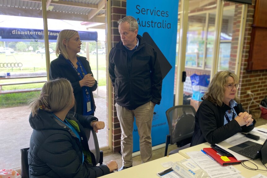 A blonde woman talks to a politician in front of a Services Australia sign.