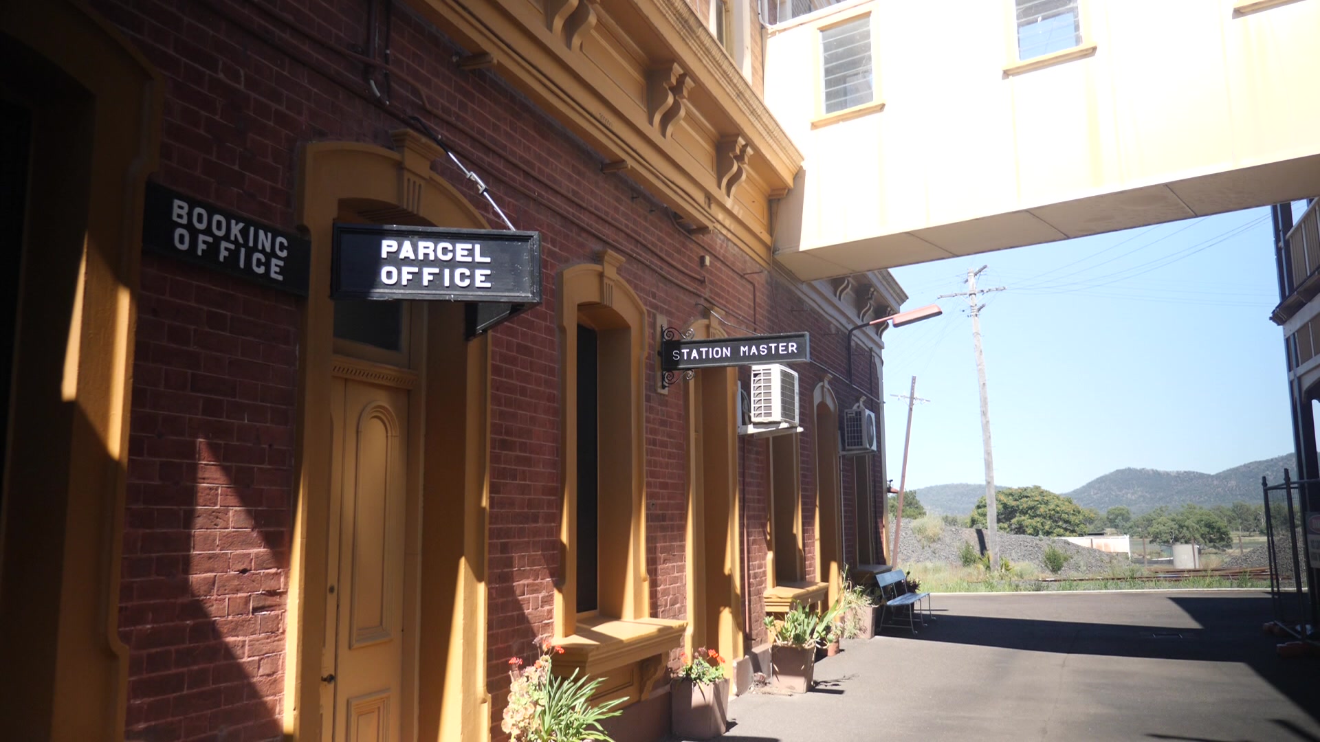 A fachada de uma estação ferroviária de tijolos com placas dizendo "chefe da estação", "escritório de encomendas" e "Escritório de reservas".