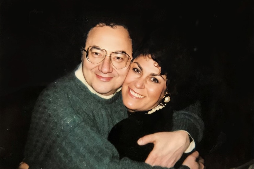 A man wraps his arms around a grinning woman