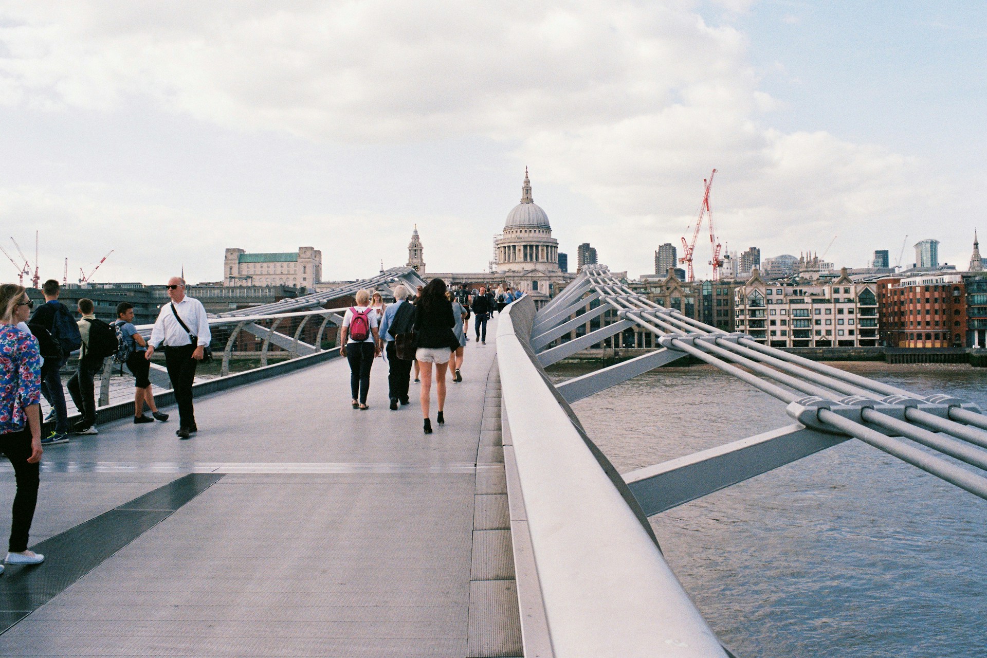People walking across the Millennium Bridge over the Thames toward St Paul's Cathedral in London.
