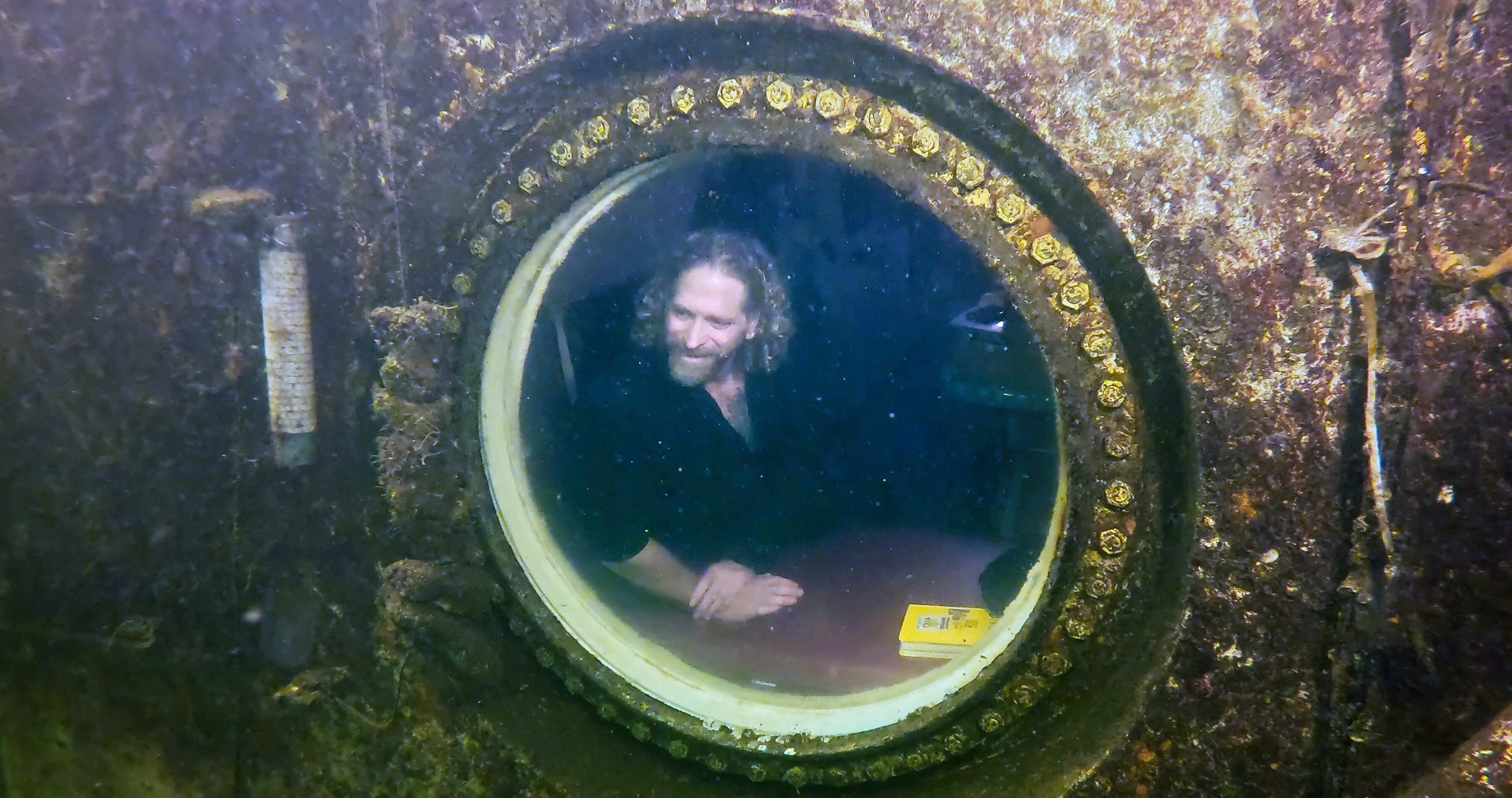 A man looking out a circle window in an underwater home. 