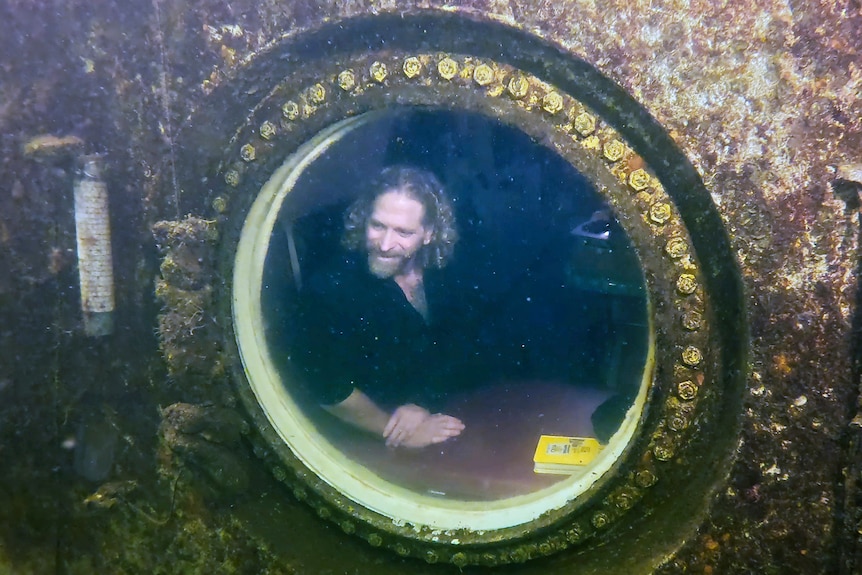 A man looking out a circle window in an underwater home. 