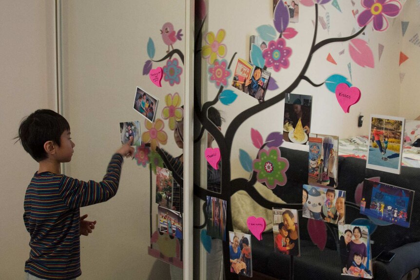 Lucas Cheang stands in front of a mirror with a memory tree of photos of his mum