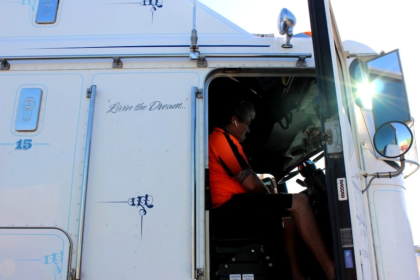 A man sits in a truck with the door open.