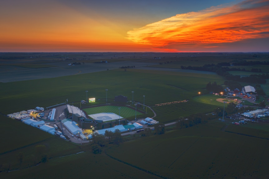 A baseball field is shown with a sunset in the background