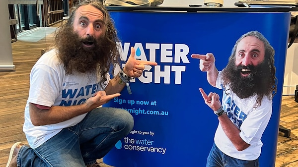 Costa kneeling in front of and pointing to a Water Week Poster with his image on it.