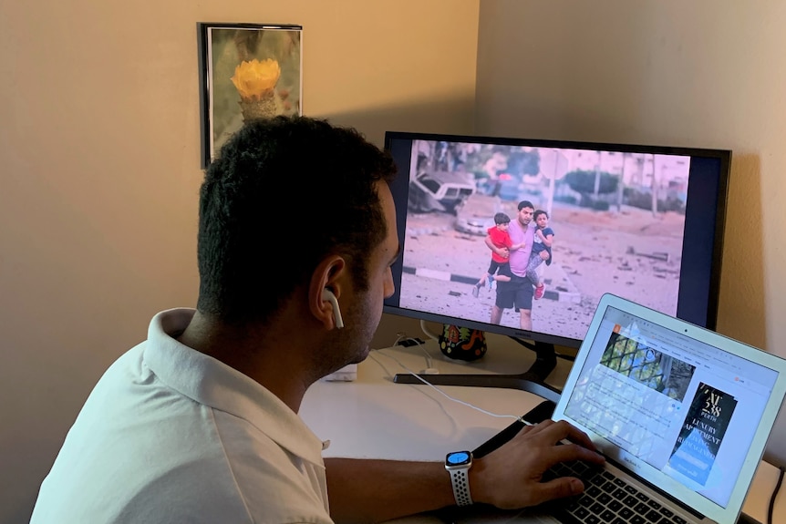 A photo of Ayman with his back facing the camera looking at news of the conflict. 
