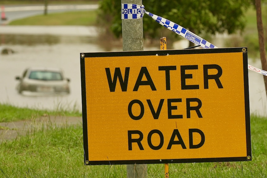 'Water over road' sign at with car in floodwaters at Rocklea