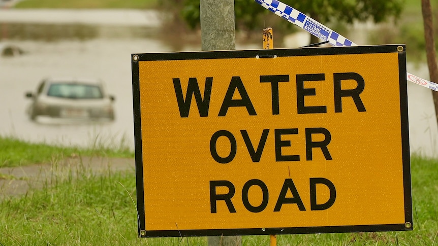 'Water over road' sign at with car in floodwaters at Rocklea