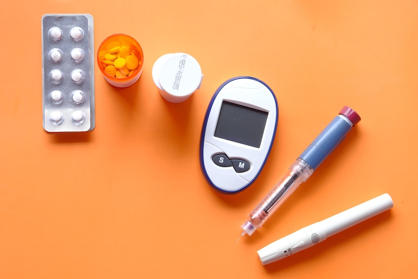 Insulin pen, diabetic measurement tools and pills on orange background