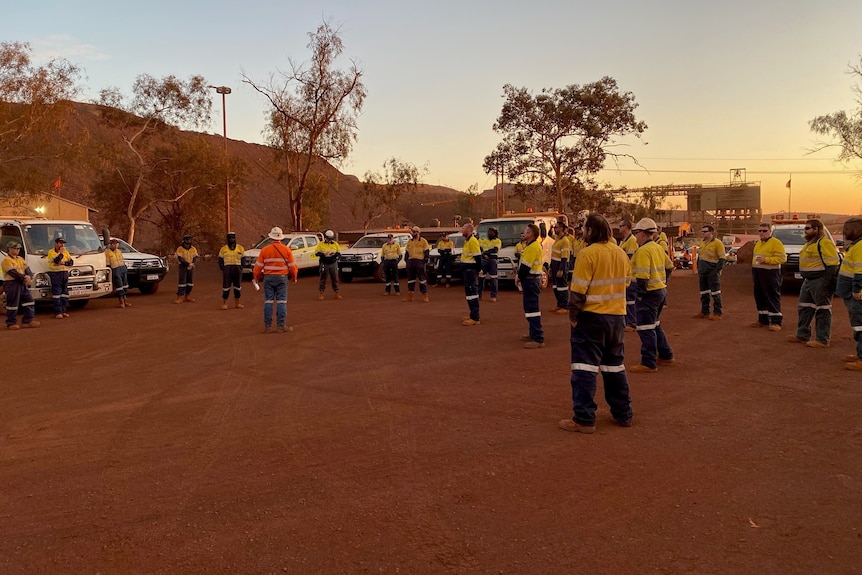 Workers gathered for a socially distanced outdoor mine meeting at sunrise.